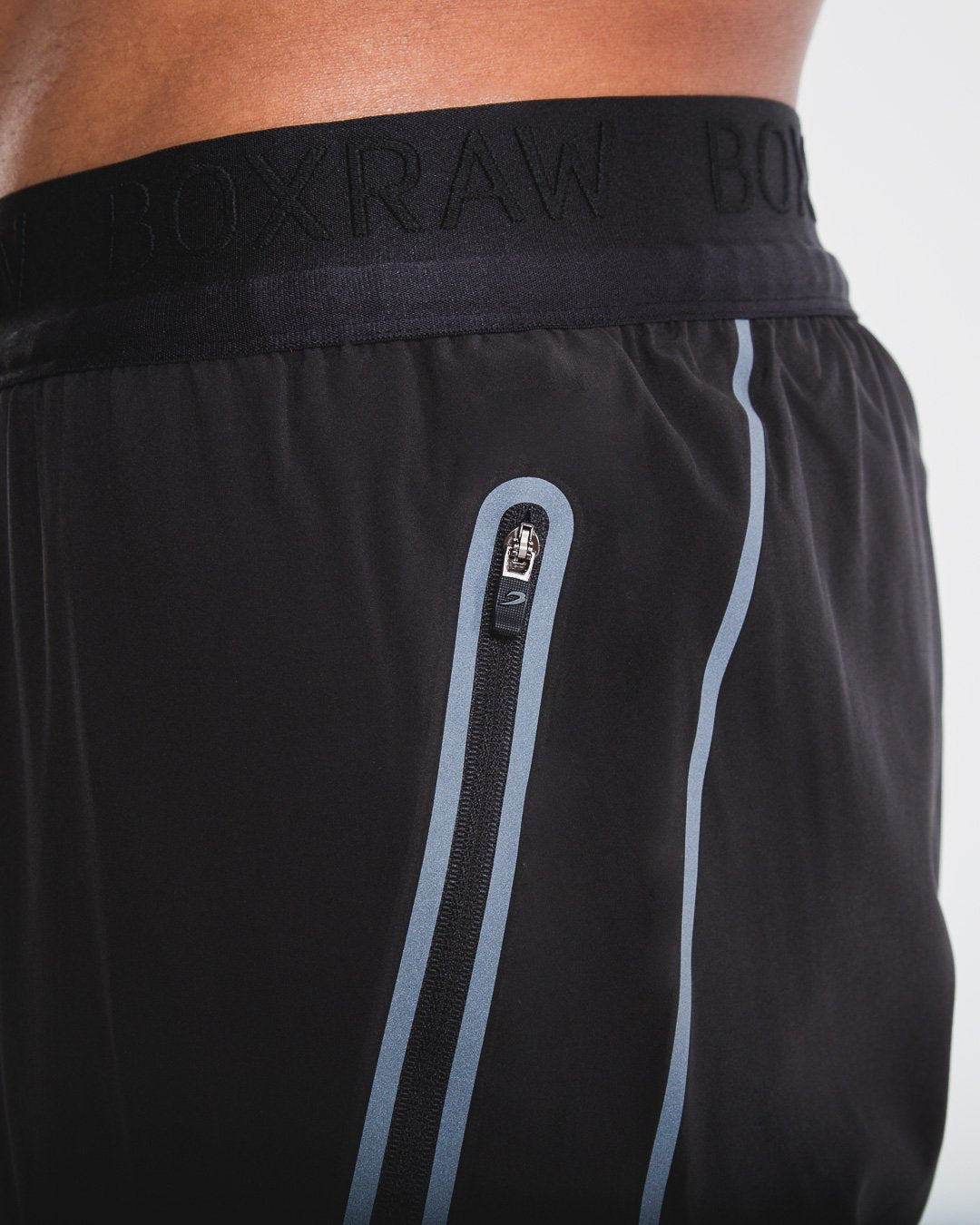Man in slim fitting black lightweight tracksuit bottoms with reflective detailing and side zipped pockets