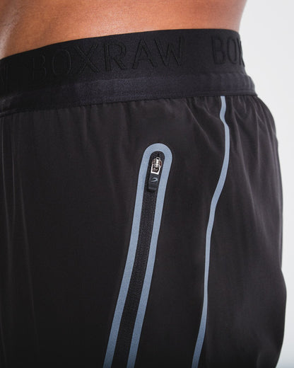 Man in slim fitting black lightweight tracksuit bottoms with reflective detailing and side zipped pockets