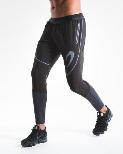 Man in slim fitting black lightweight tracksuit bottoms with reflective detailing and side zipped pockets
