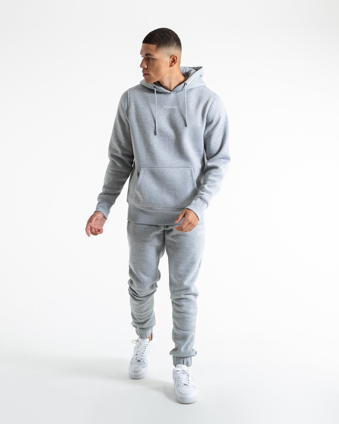 Man in relaxed fit grey tracksuit bottoms with a white 3D boxraw logo as well as side zipped pockets made from a cotton/poly blend.
