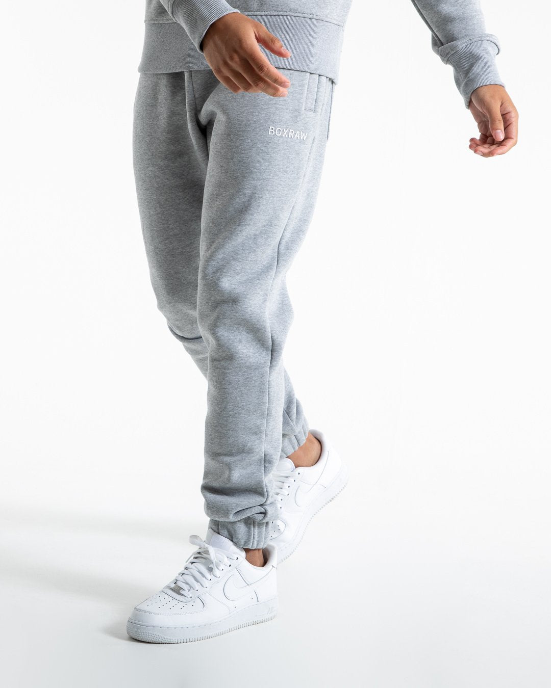Man in relaxed fit grey tracksuit bottoms with a white 3D boxraw logo as well as side zipped pockets made from a cotton/poly blend.