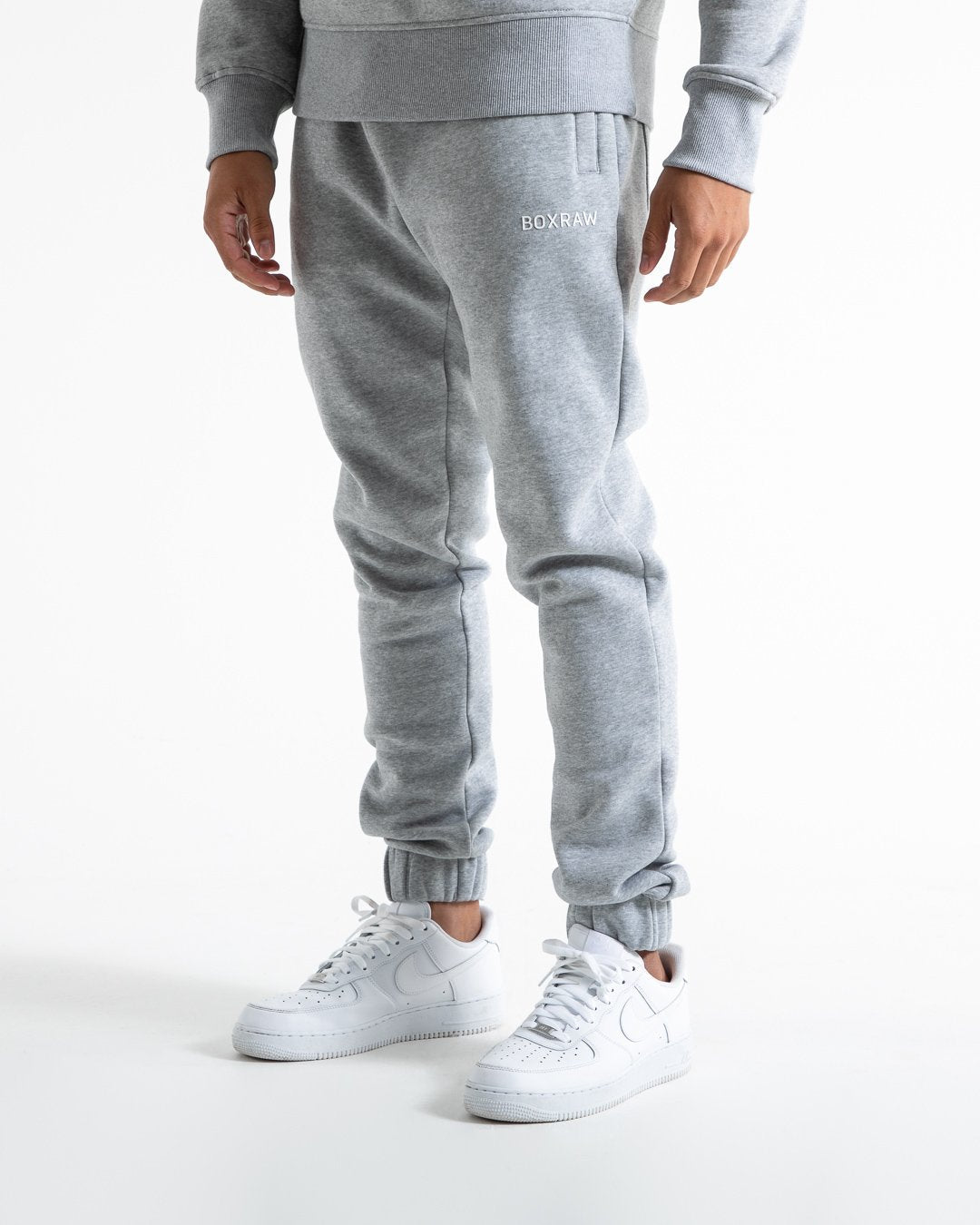 Man in relaxed fit grey tracksuit bottoms with a white 3D boxraw logo as well as side zipped pockets made from a cotton/poly blend.