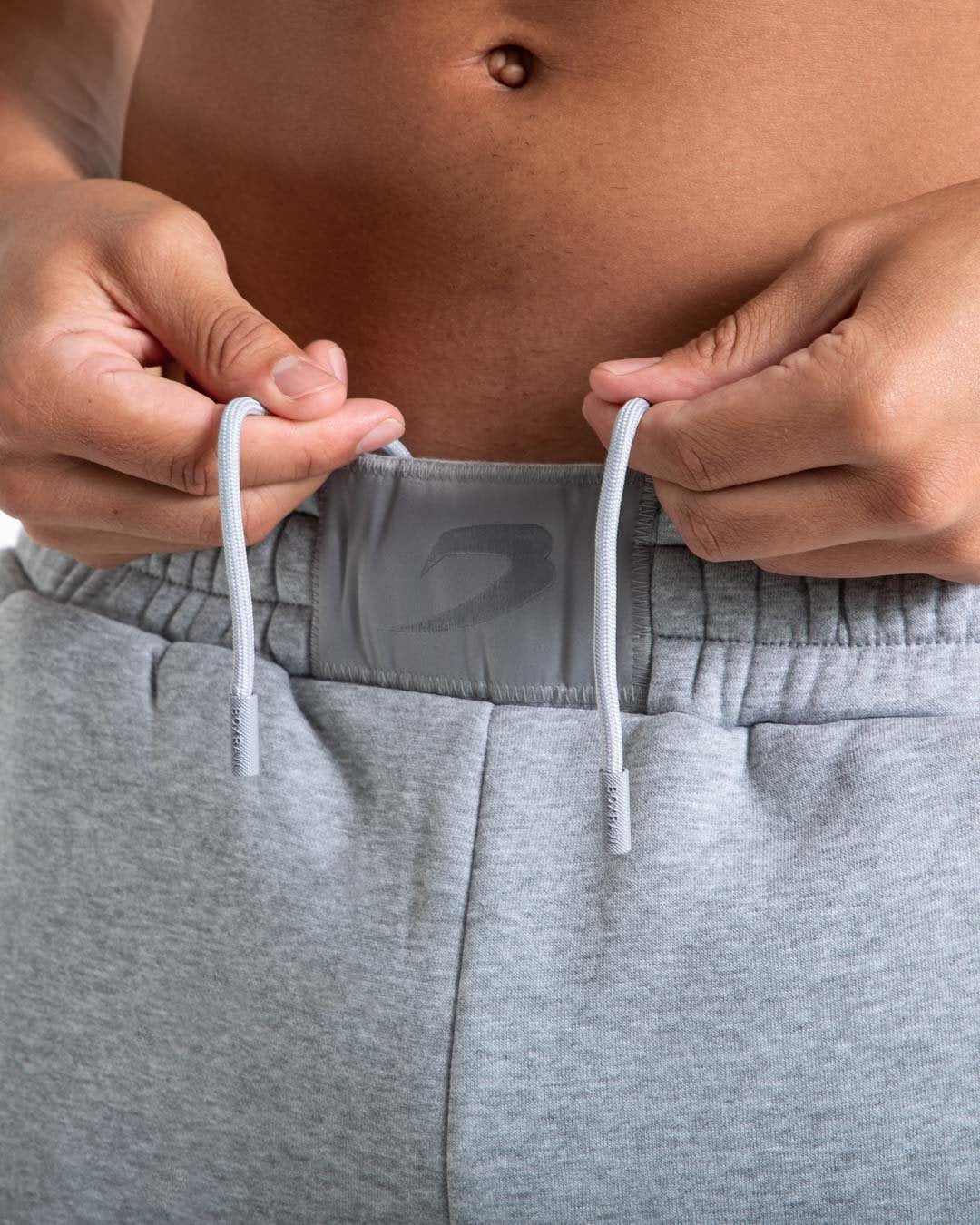 Man in relaxed fit grey tracksuit bottoms with a white 3D boxraw logo as well as side zipped pockets made from a cotton/poly blend.