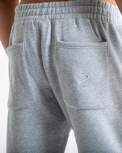 Man in relaxed fit grey tracksuit bottoms with a white 3D boxraw logo as well as side zipped pockets made from a cotton/poly blend.