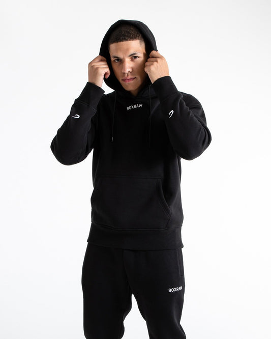 Man in black jumper with hood and kangaroo pouch as well as white 3D boxraw logo on the chest and embroidered strike logos on sleeves.