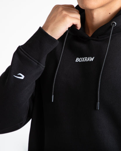 Man in black jumper with hood and kangaroo pouch as well as white 3D boxraw logo on the chest and embroidered strike logos on sleeves.