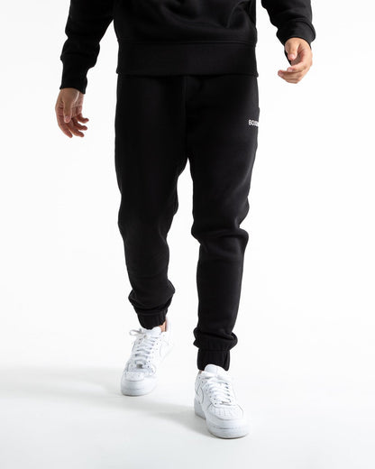 Man in relaxed fit black tracksuit bottoms with a white 3D boxraw logo as well as side zipped pockets made from a cotton/poly blend.