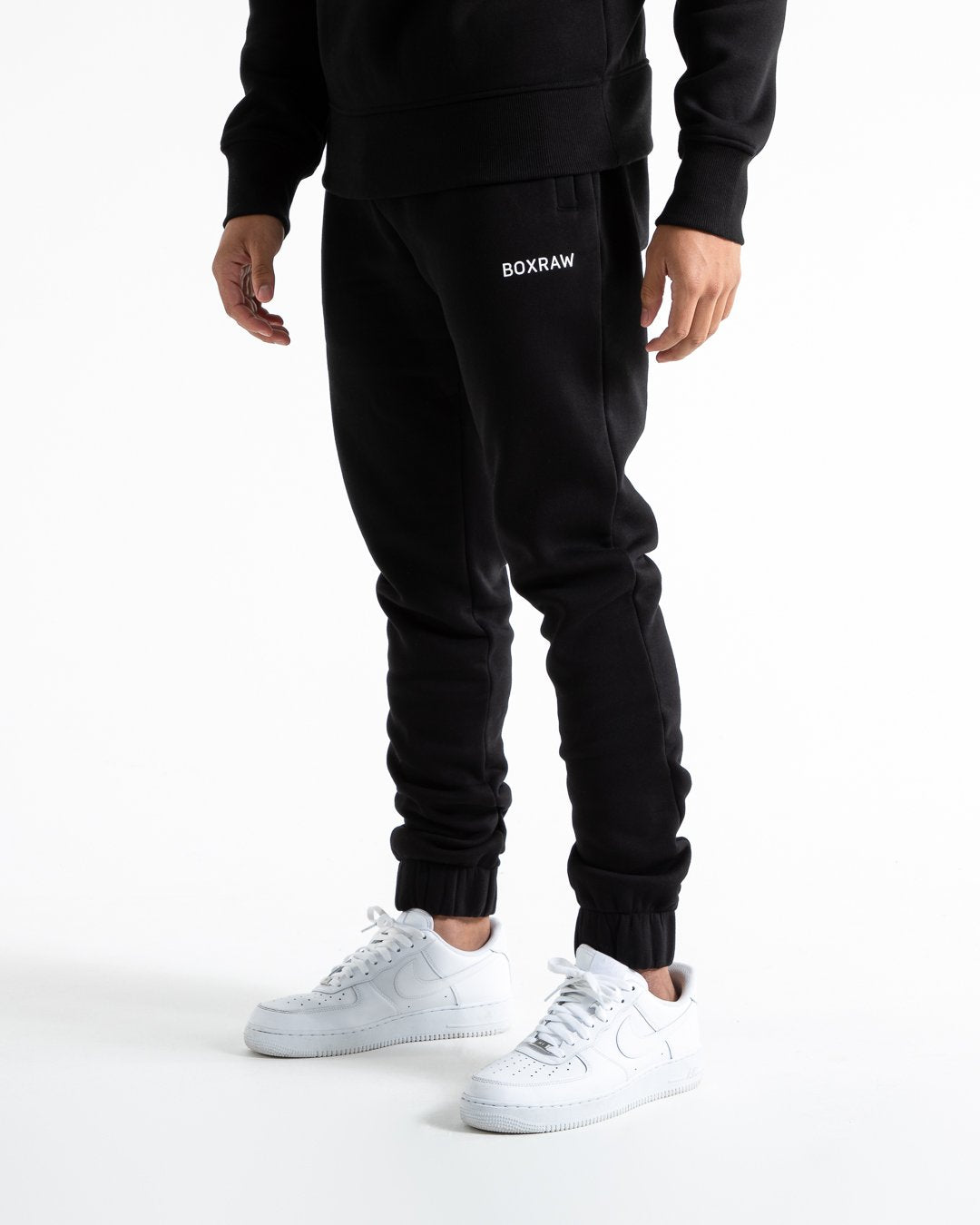 Man in relaxed fit black tracksuit bottoms with a white 3D boxraw logo as well as side zipped pockets made from a cotton/poly blend.