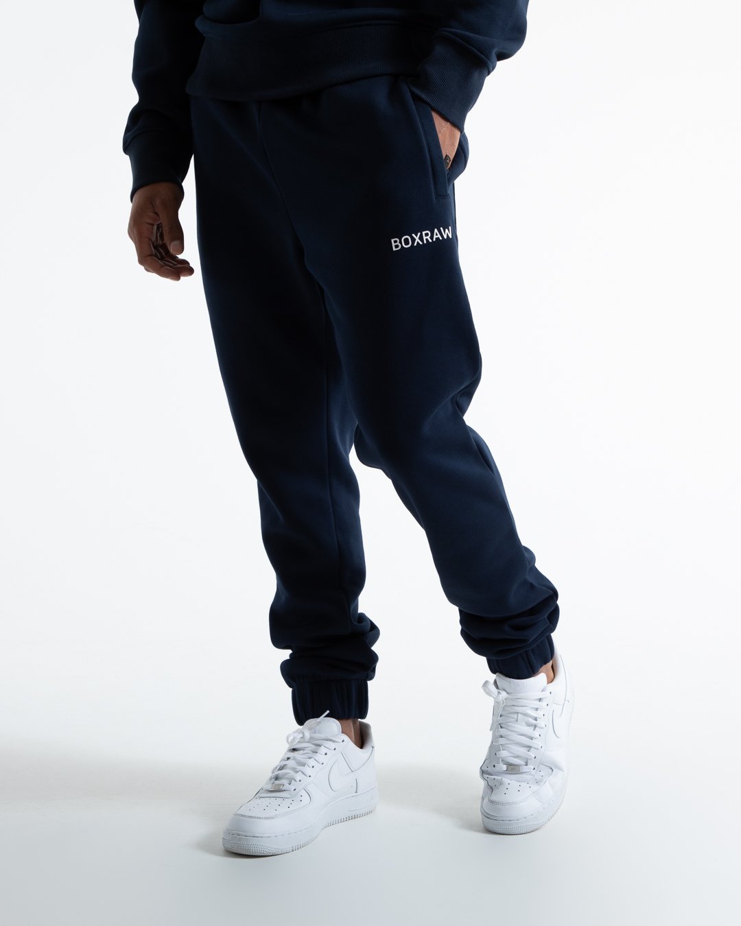 Man in relaxed fit navy tracksuit bottoms with a white 3D boxraw logo as well as side zipped pockets made from a cotton/poly blend.