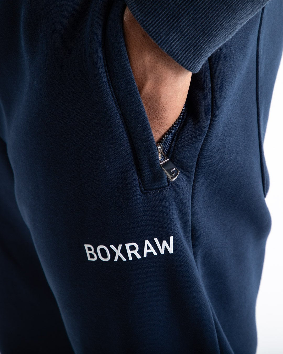 Man in relaxed fit navy tracksuit bottoms with a white 3D boxraw logo as well as side zipped pockets made from a cotton/poly blend.