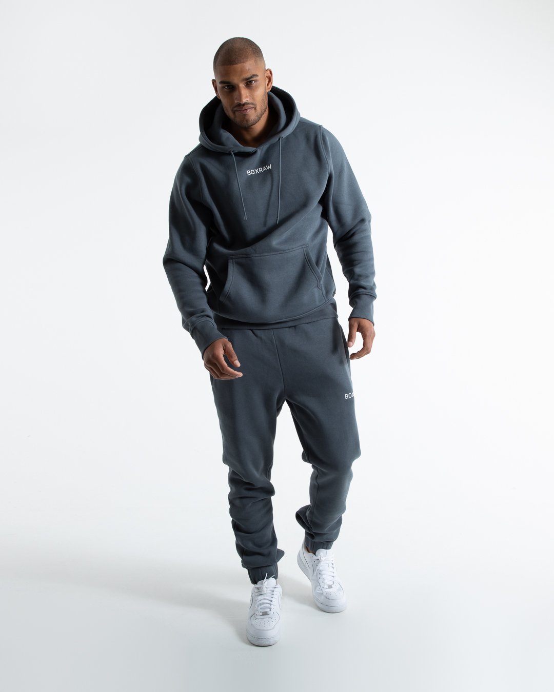 Man in relaxed fit charcoal tracksuit bottoms with a white 3D boxraw logo as well as side zipped pockets made from a cotton/poly blend.