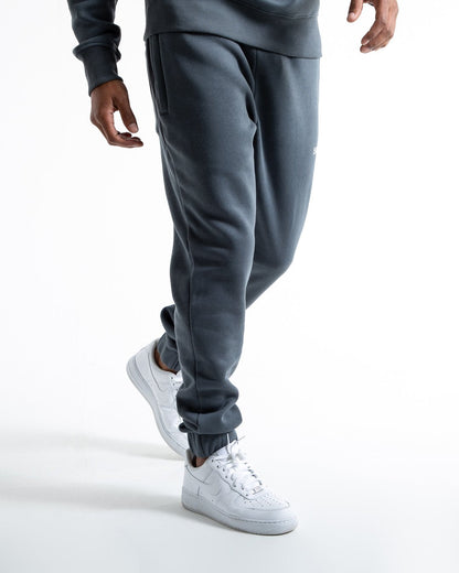 Man in relaxed fit charcoal tracksuit bottoms with a white 3D boxraw logo as well as side zipped pockets made from a cotton/poly blend.
