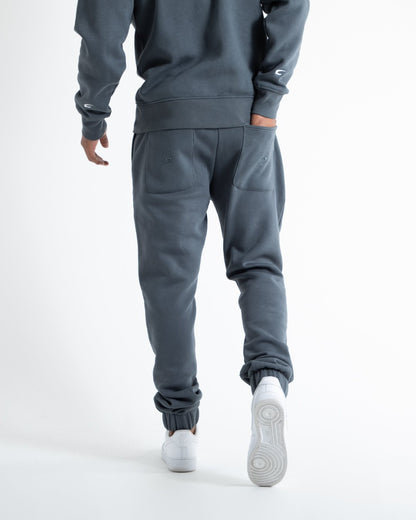 Man in relaxed fit charcoal tracksuit bottoms with a white 3D boxraw logo as well as side zipped pockets made from a cotton/poly blend.