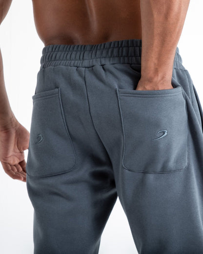 Man in relaxed fit charcoal tracksuit bottoms with a white 3D boxraw logo as well as side zipped pockets made from a cotton/poly blend.