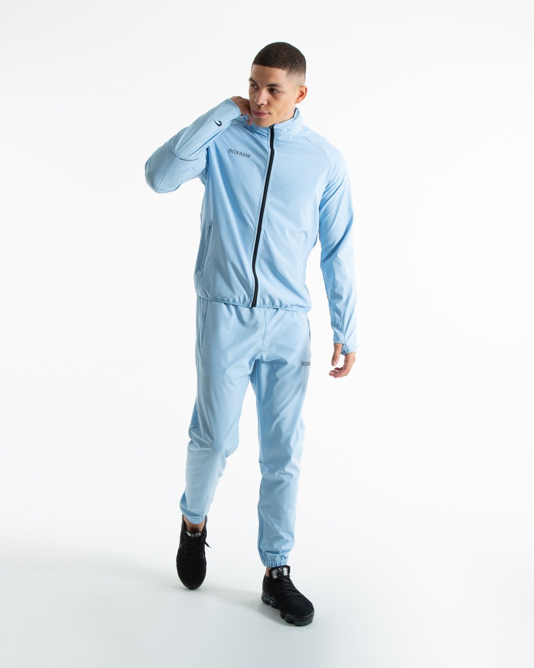 Man in baby blue lightweight tracksuit bottoms with mesh/perforated ventilation panels on the legs with black boxraw logo