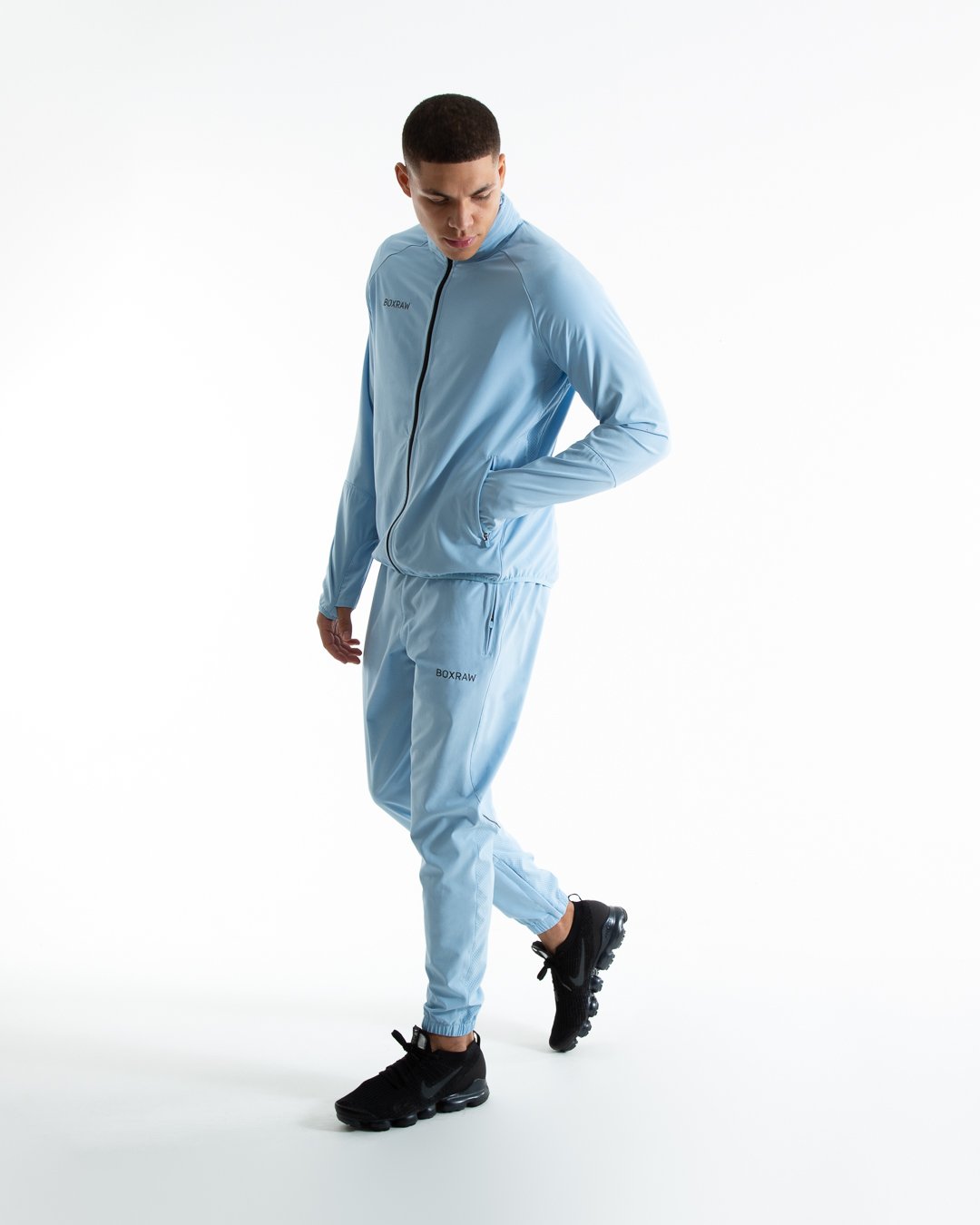 Man in baby blue zipped lightweight tracksuit jacket with a hidden zipped hoodie with black boxraw logo made from polyester.