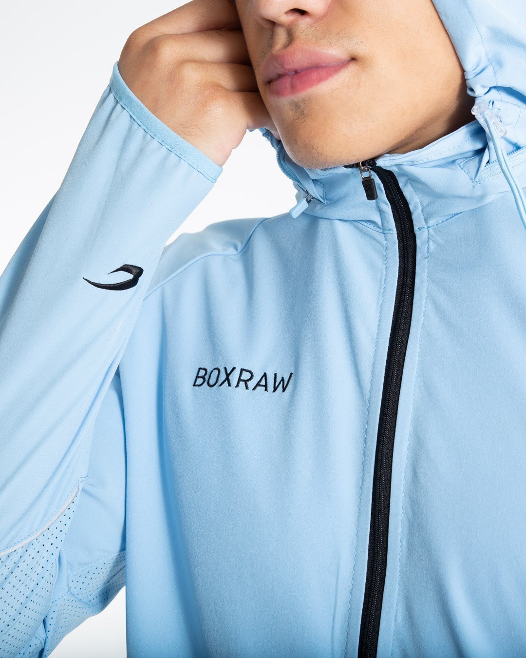 Man in baby blue zipped lightweight tracksuit jacket with a hidden zipped hoodie with black boxraw logo made from polyester.