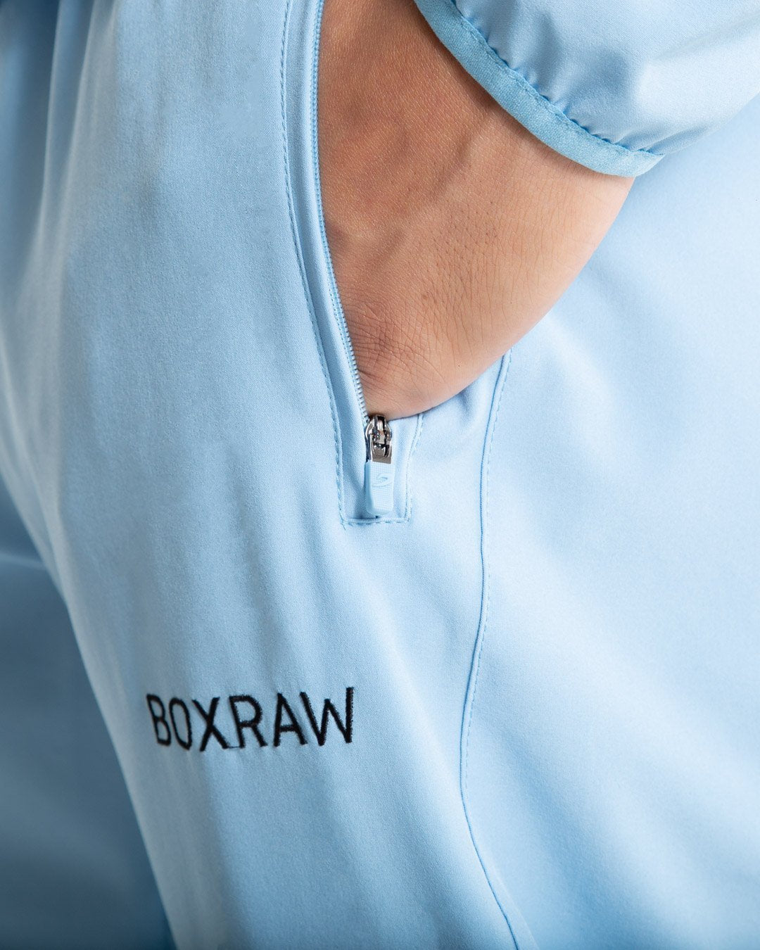 Man in baby blue lightweight tracksuit bottoms with mesh/perforated ventilation panels on the legs with black boxraw logo