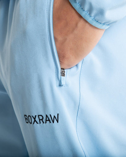 Man in baby blue lightweight tracksuit bottoms with mesh/perforated ventilation panels on the legs with black boxraw logo