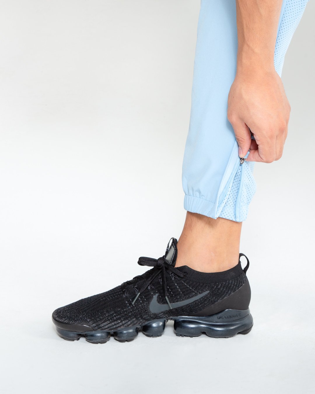 Man in baby blue lightweight tracksuit bottoms with mesh/perforated ventilation panels on the legs with black boxraw logo