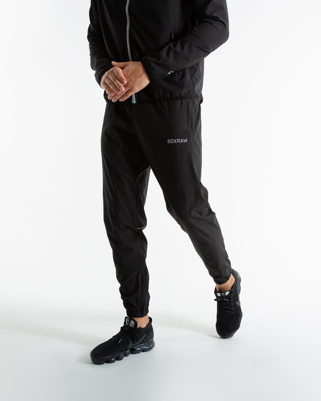 Man in black lightweight tracksuit bottoms with mesh/perforated ventilation panels on the legs with white boxraw logo.