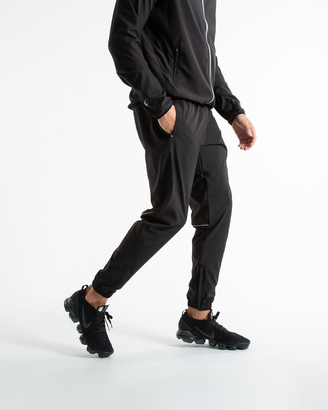 Man in black lightweight tracksuit bottoms with mesh/perforated ventilation panels on the legs with white boxraw logo.