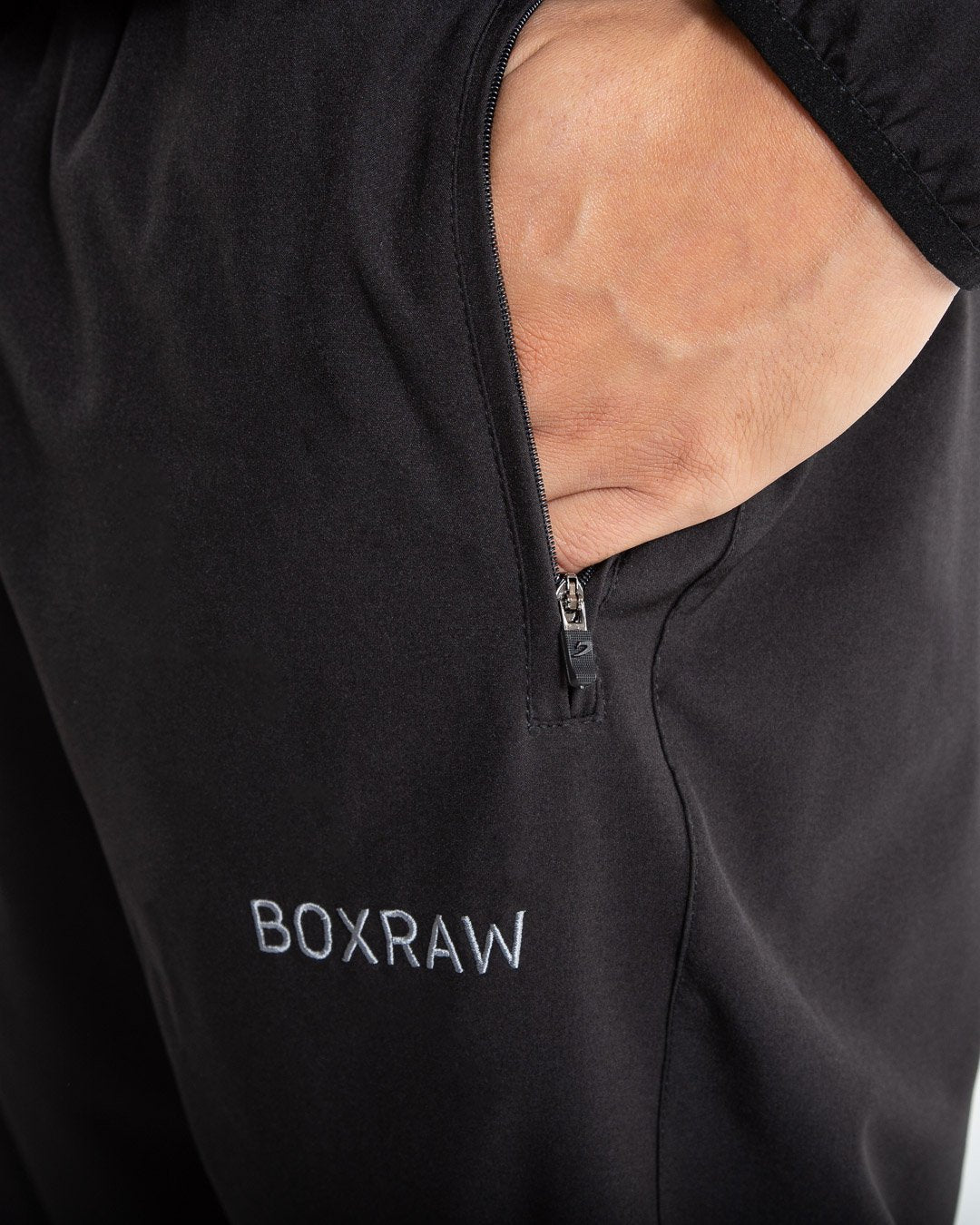 Man in black lightweight tracksuit bottoms with mesh/perforated ventilation panels on the legs with white boxraw logo.