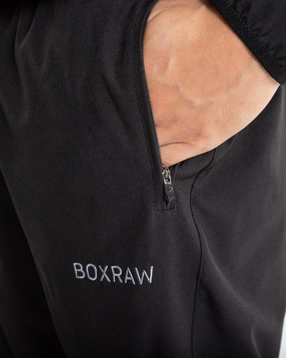 Man in black lightweight tracksuit bottoms with mesh/perforated ventilation panels on the legs with white boxraw logo.