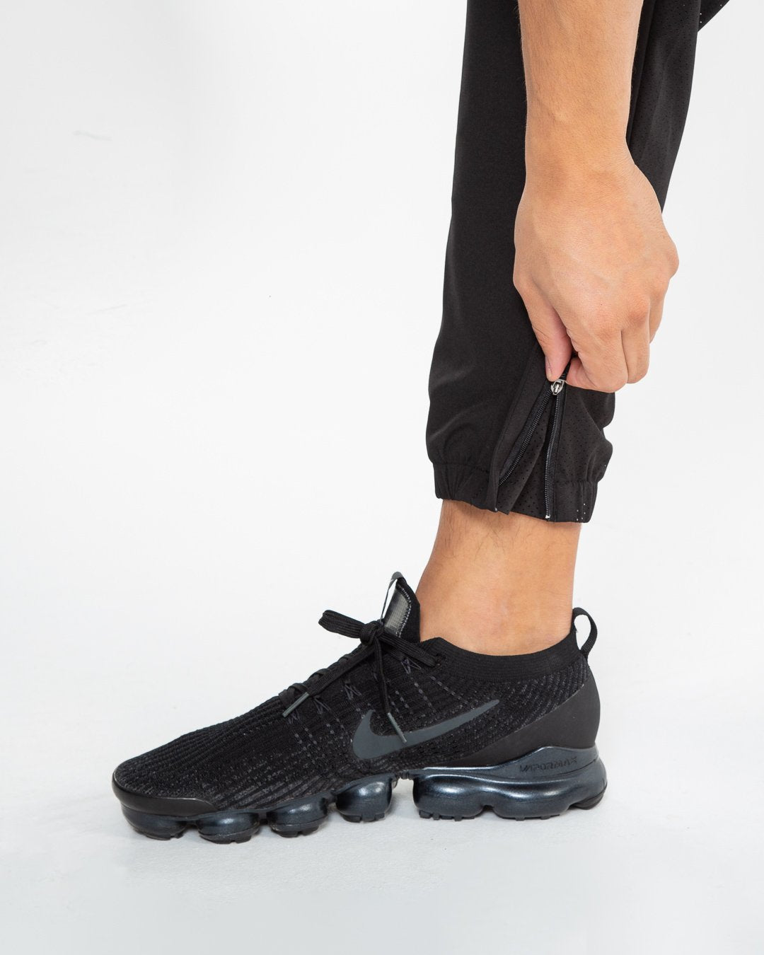 Man in black lightweight tracksuit bottoms with mesh/perforated ventilation panels on the legs with white boxraw logo.