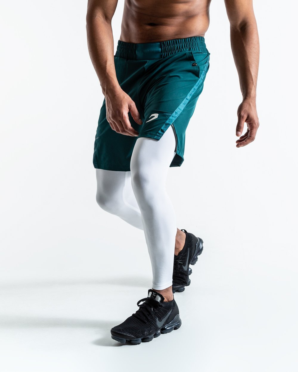 Man in green training shorts made from polyester with white compression leggings inside made from cotton with deep side pocket with a white strike logo.