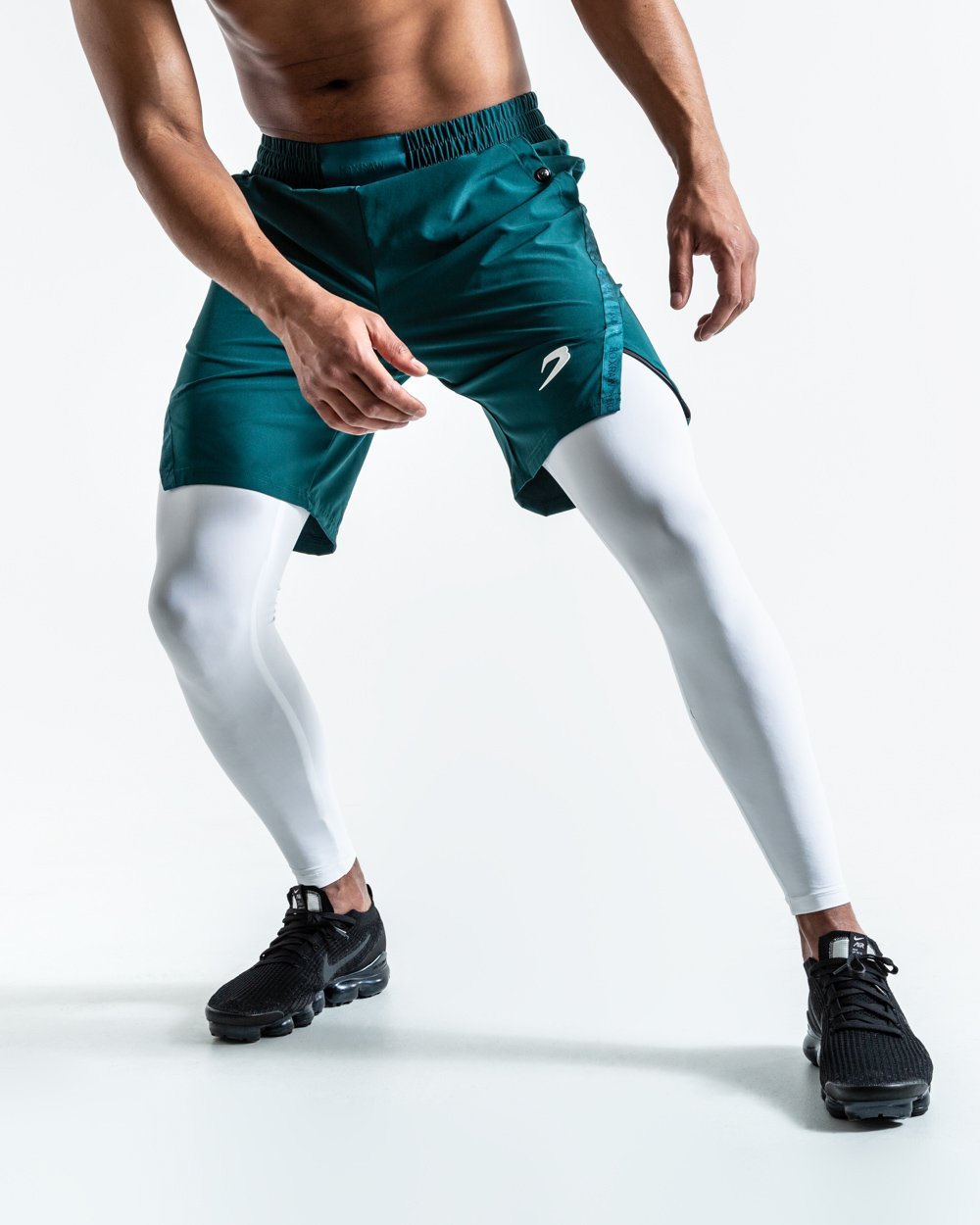 Man in green training shorts made from polyester with white compression leggings inside made from cotton with deep side pocket with a white strike logo.