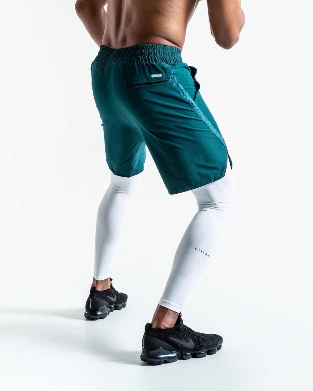 Man in green training shorts made from polyester with white compression leggings inside made from cotton with deep side pocket with a white strike logo.