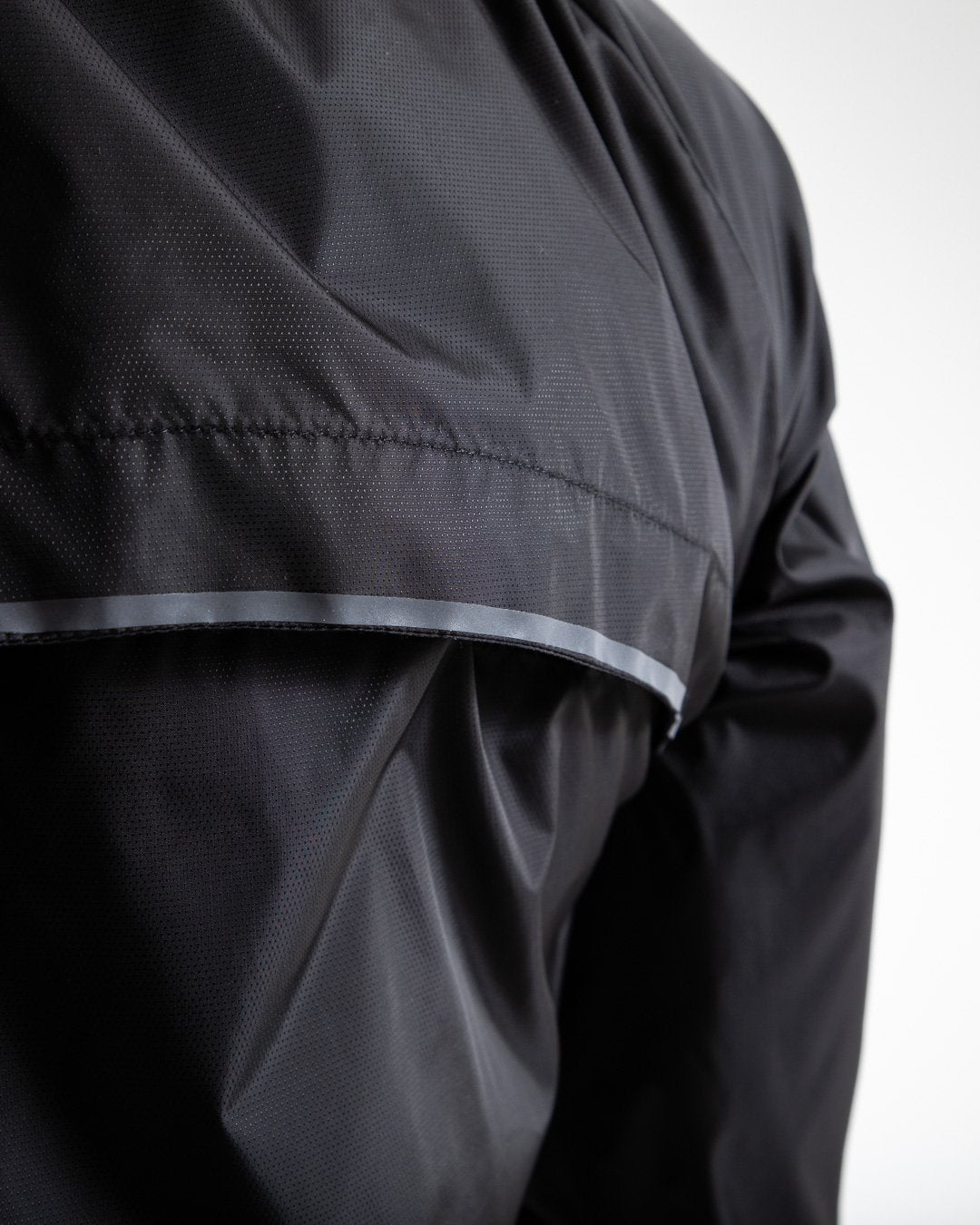 Man in black zipped windbreaker with hood and reflective big boxraw strike logo across left body panel made from nylon.