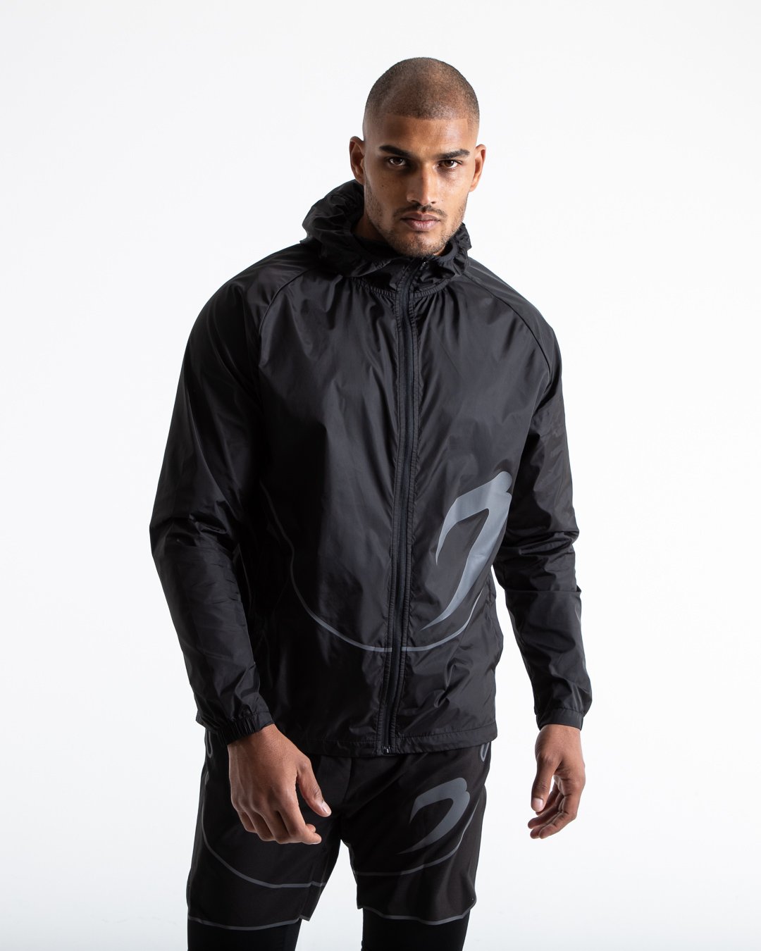 Man in black zipped windbreaker with hood and reflective big boxraw strike logo across left body panel made from nylon.