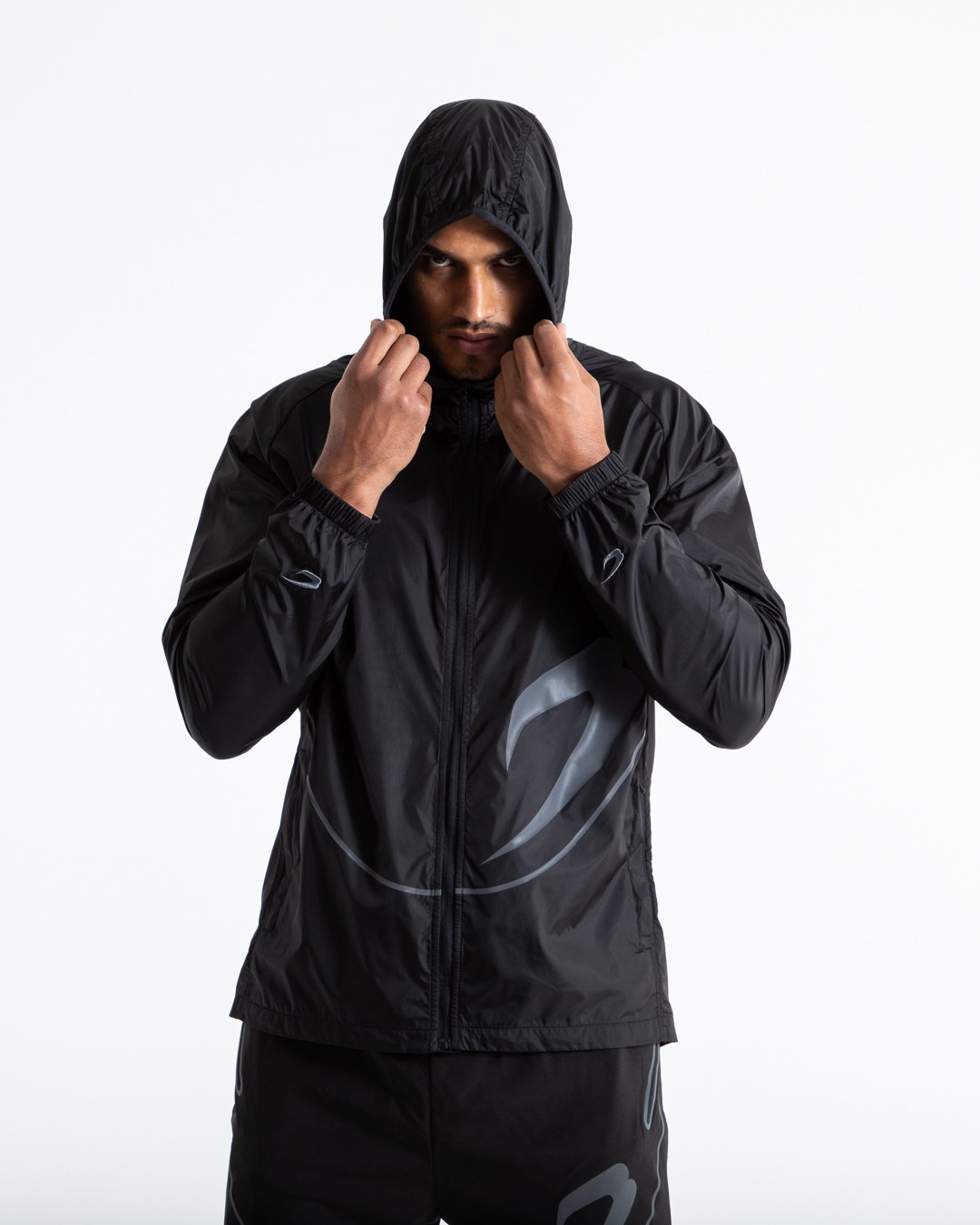 Man in black zipped windbreaker with hood and reflective big boxraw strike logo across left body panel made from nylon.