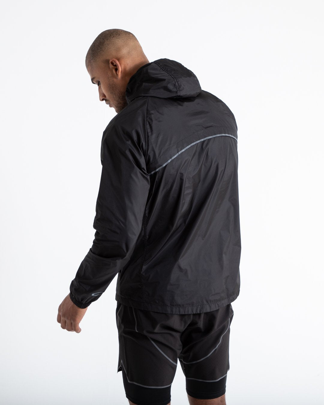 Man in black zipped windbreaker with hood and reflective big boxraw strike logo across left body panel made from nylon.