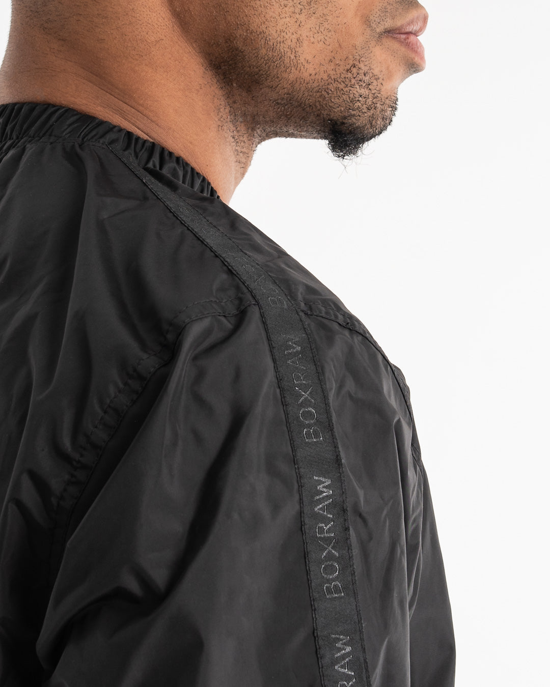 Man in a black sauna suit tracksuit with a white boxraw logo on the chest as well as adjustable wrist straps and made from polyester.