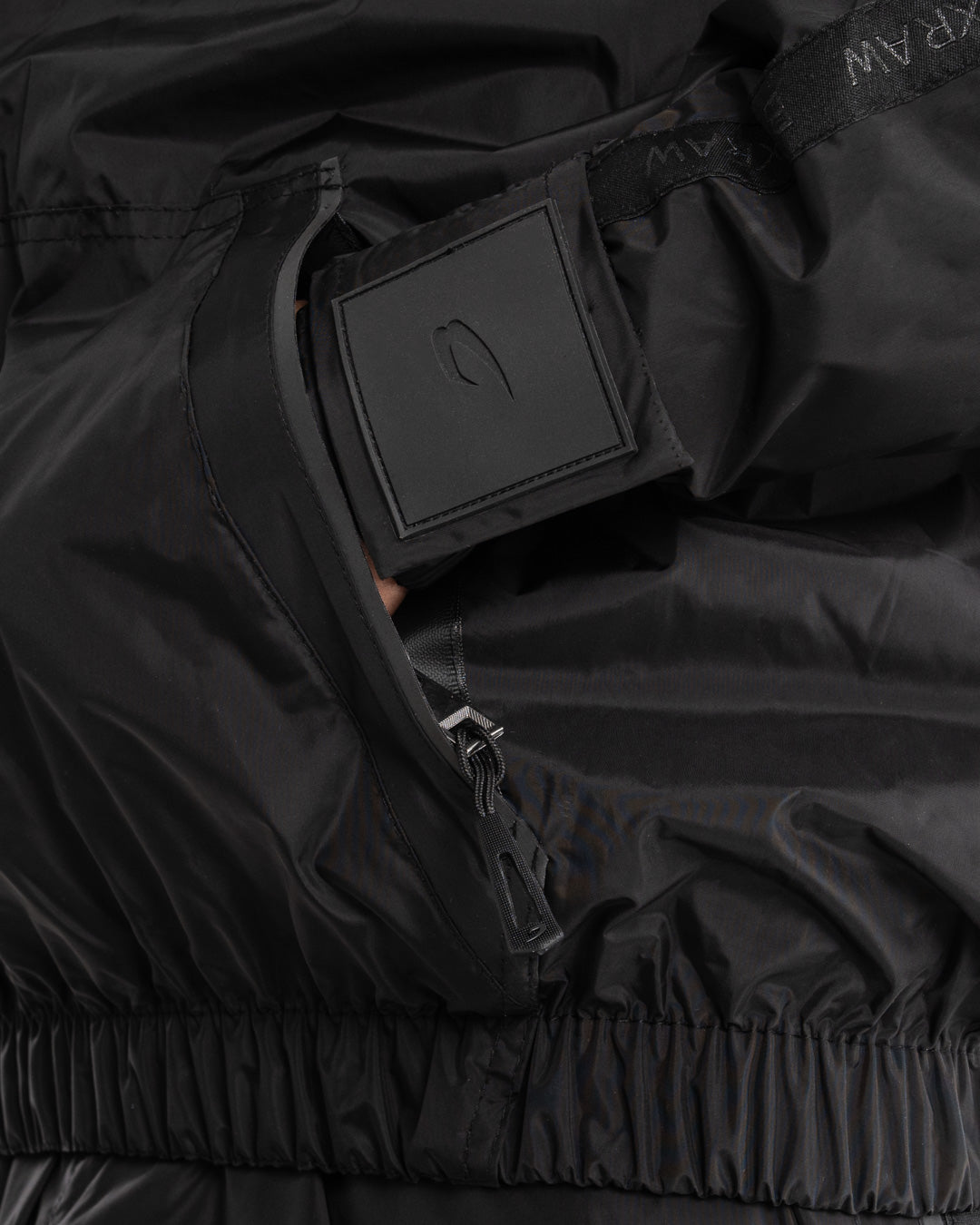 Man in a black sauna suit tracksuit with a white boxraw logo on the chest as well as adjustable wrist straps and made from polyester.