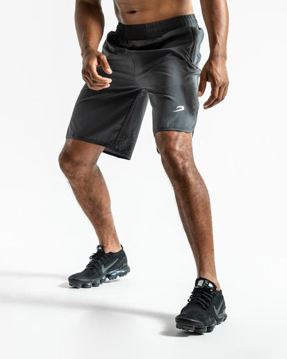 Man in charcoal training shorts with adjustable waistband and side zipped pockets as well as an embroidered white boxraw strike logo.