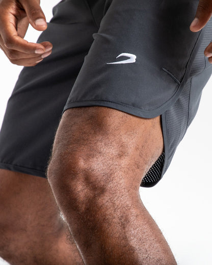 Man in charcoal training shorts with adjustable waistband and side zipped pockets as well as an embroidered white boxraw strike logo.