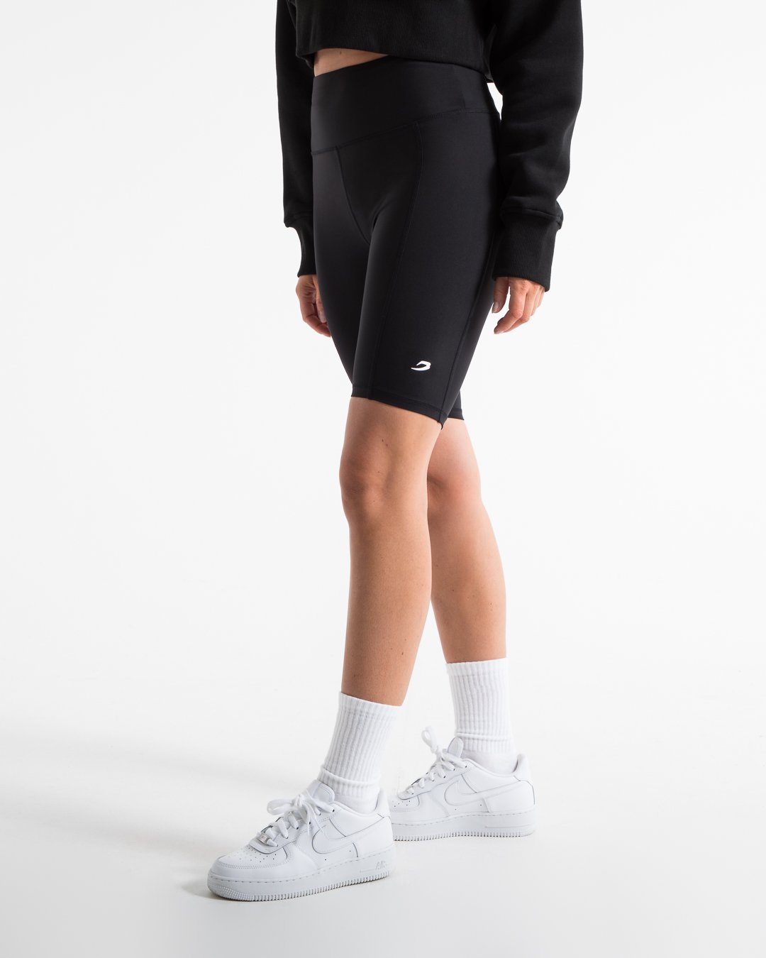 Women in black high wasted cycling shorts with a compressed fit and hidden side pockets as well as a 3D white strike logo