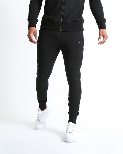 Man in black slim fit tracksuit bottoms with metal strike logo and zipped side pockets