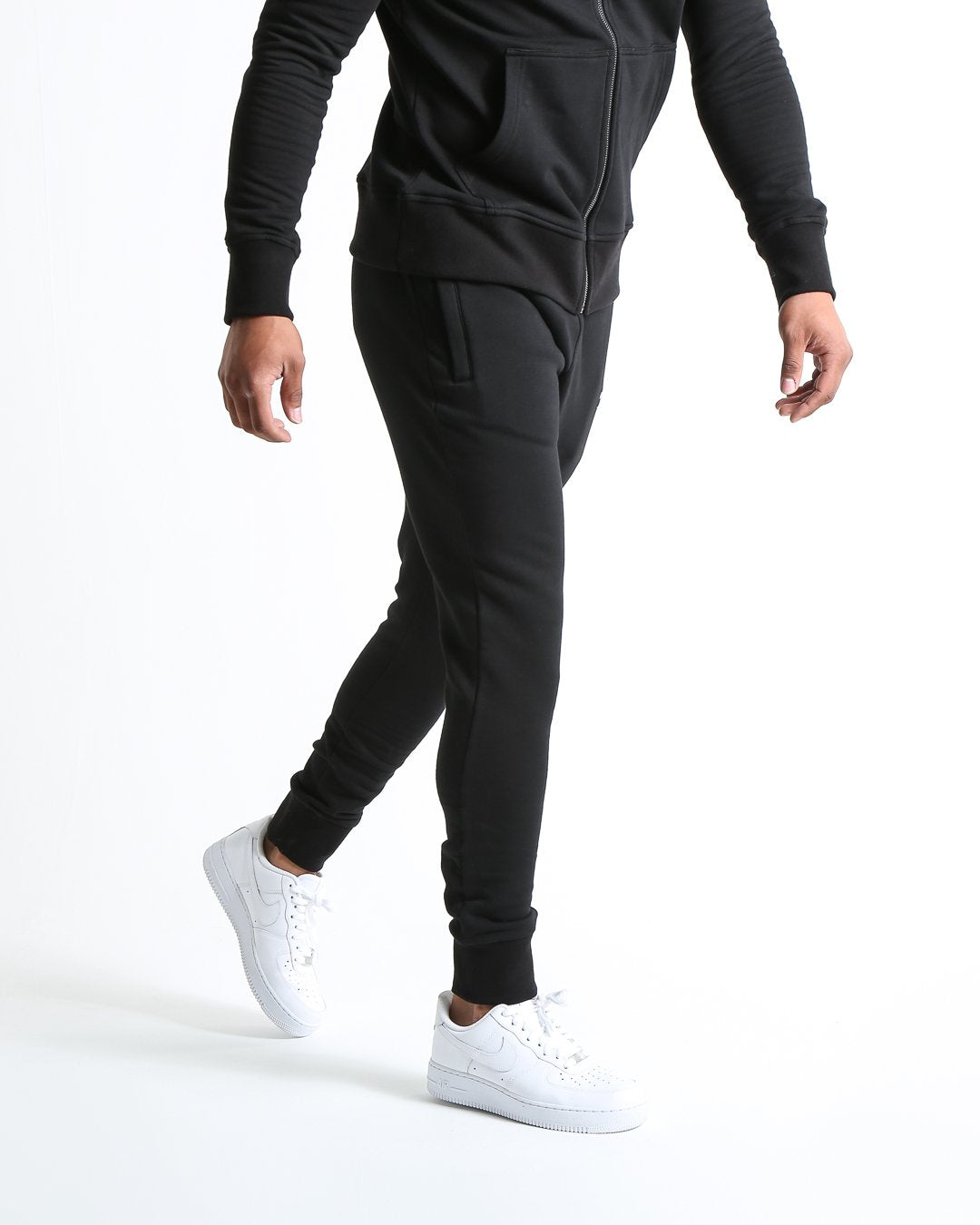 Man in black slim fit tracksuit bottoms with metal strike logo and zipped side pockets