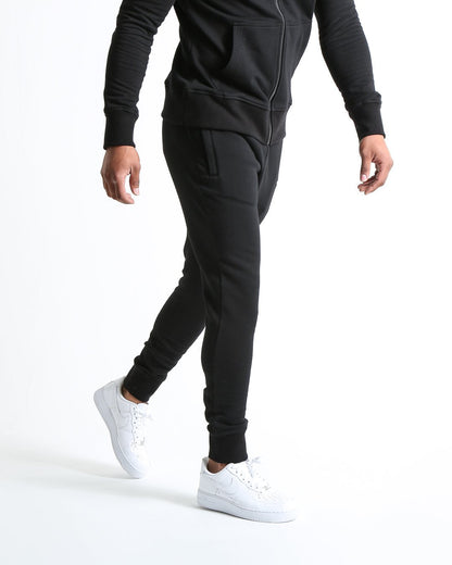 Man in black slim fit tracksuit bottoms with metal strike logo and zipped side pockets