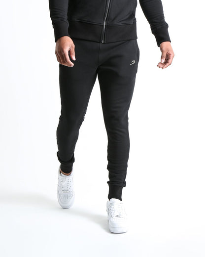 Man in black slim fit tracksuit bottoms with metal strike logo and zipped side pockets
