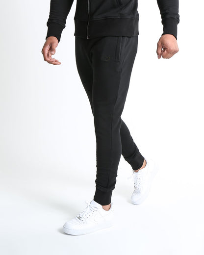 Man in black slim fit tracksuit bottoms with metal strike logo and zipped side pockets
