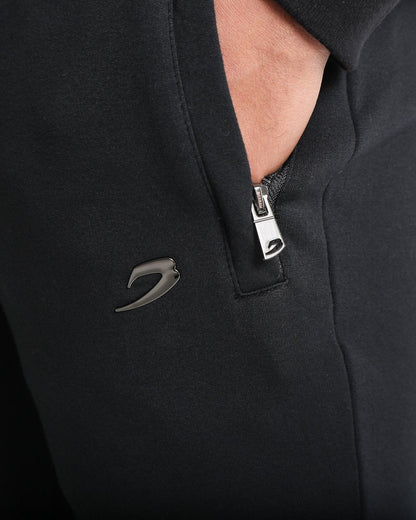 Man in black slim fit tracksuit bottoms with metal strike logo and zipped side pockets